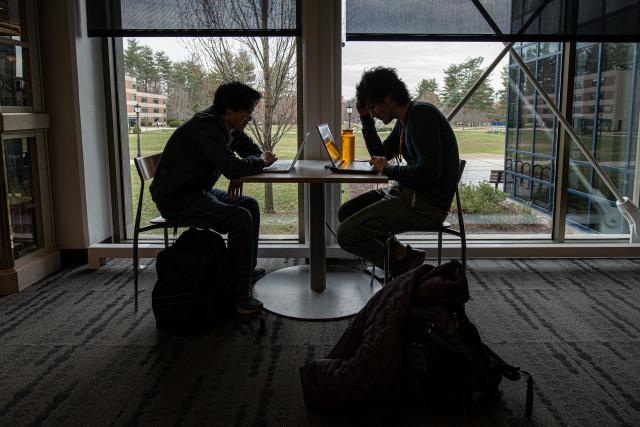 Two students study in silhouette by the windows of the campus center
