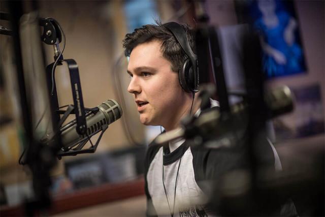 A student wearing headphones talks into a professional microphone.