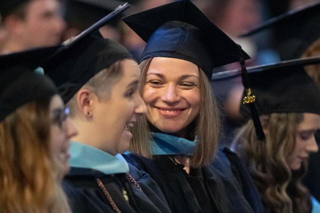  Multiple students wearing their caps and gowns smile during their graduation ceremony.