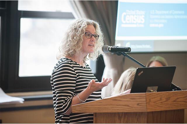 A professor presents coursework while standing at a podium in a classroom setting.