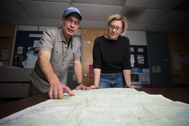 Two people look over a large map that is spread out on a table.