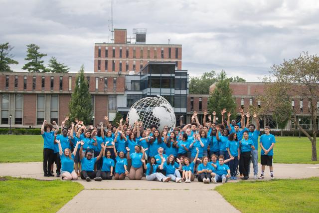 Urban Education group photo in front of campus globe with students wearing blue tee shirts.