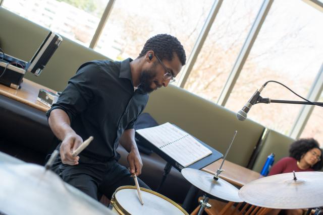 Music student wearing glasses drumming at jazz brunch event.