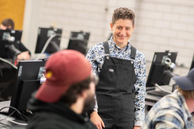 Data science faculty member smiling in classroom wearing black overalls and blue shirt.