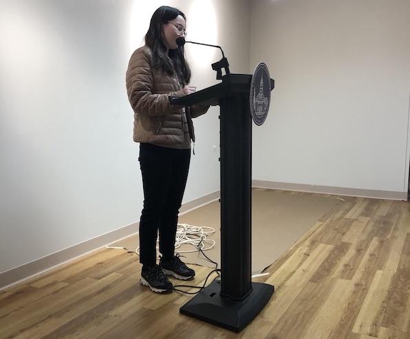 Alexis Crafts, a student reading her poetry at the Chapbook Presentation event on campus on December, 16. She is wearing clear glasses, a long-sleeve gray jacket and black pants.