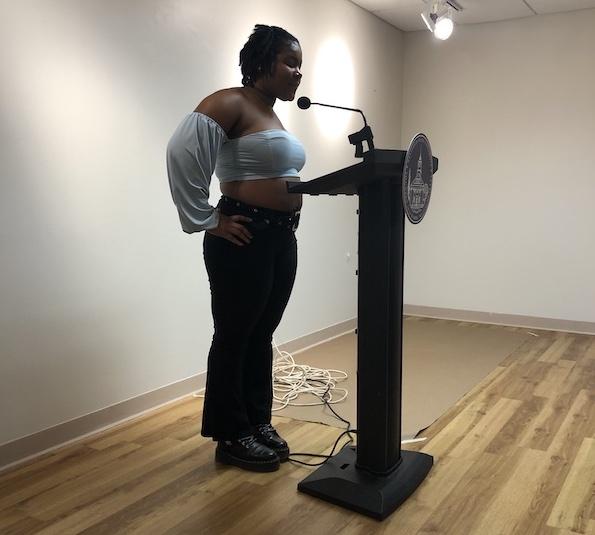 Ketia Valme, a student reading her poetry at the Chapbook Presentation event on campus on December, 16. She is wearing a long-sleeve blue top and black pants.