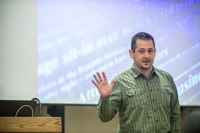 Marketing professor teaching in front of large screen wearing green button down shirt.