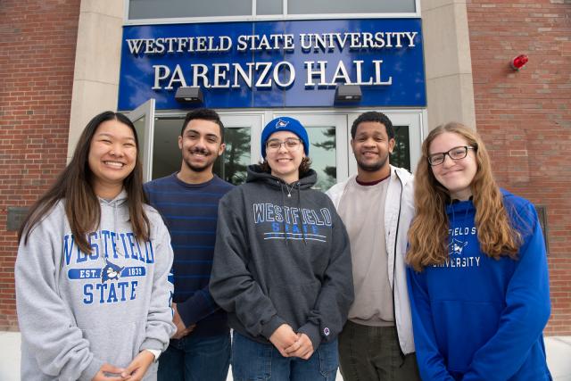 Five students wearing Westfield State sweatshirts smiling in front of Parenzo Hall.