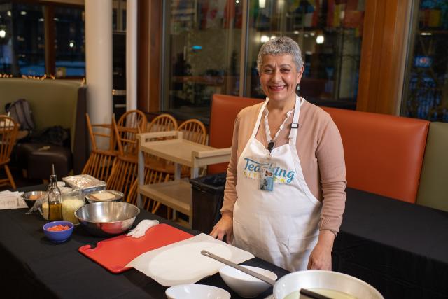 Maria from Cooking with Maria class wearing white apron smiling in Dining Commons.