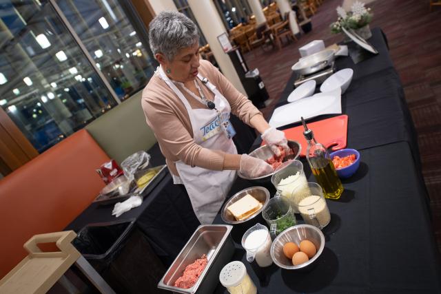 Cooking with Maria class featuring Maria in front of ingredients wearing white apron in Dining Commons.