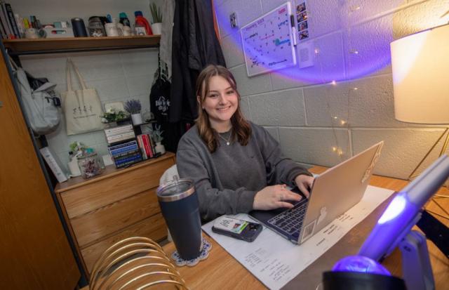 A student sits at their desk in their dorm room to work on homework.