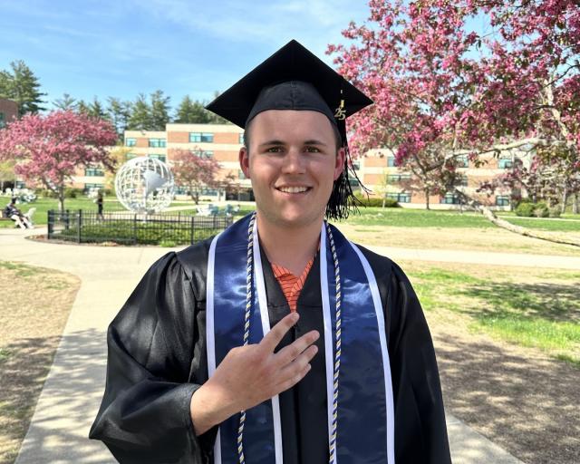 Student in cap and gown holding up four fingers to represent four days until commencement.
