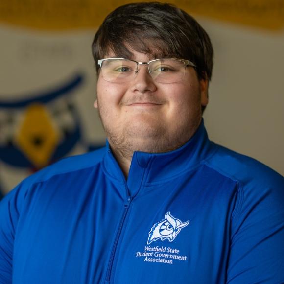 SGA Parliamentarian, Jakob wearing a blue shirt smiling.