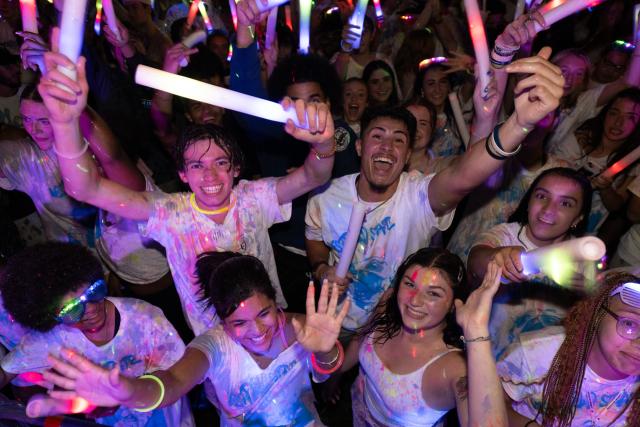 Glow party on the campus green with students smiling holding glow sticks.