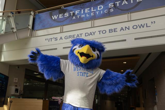 Nestor, Westfield State's owl mascot, standing beneath a sign that reads, "It's a Great Day to be an Owl."