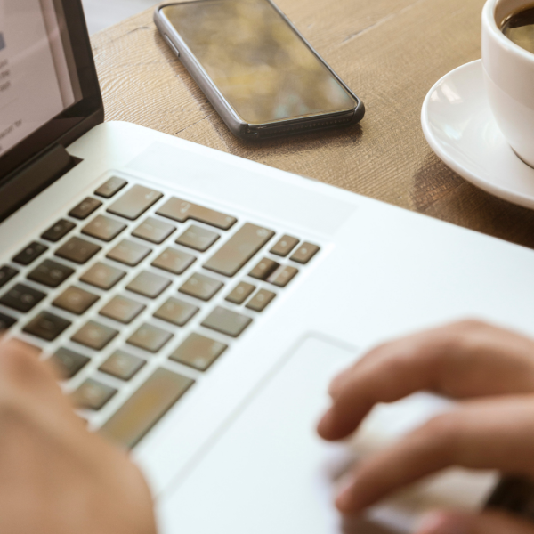 Close up of hands on the keyboard of a laptop, there is a smartphone and cup of coffee next to the laptop
