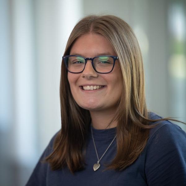 Emily smiling wearing blue shirt and glasses.