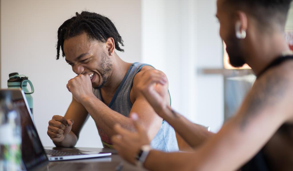 Male student laughing with friend as they work on their laptops in the Ely Campus Center