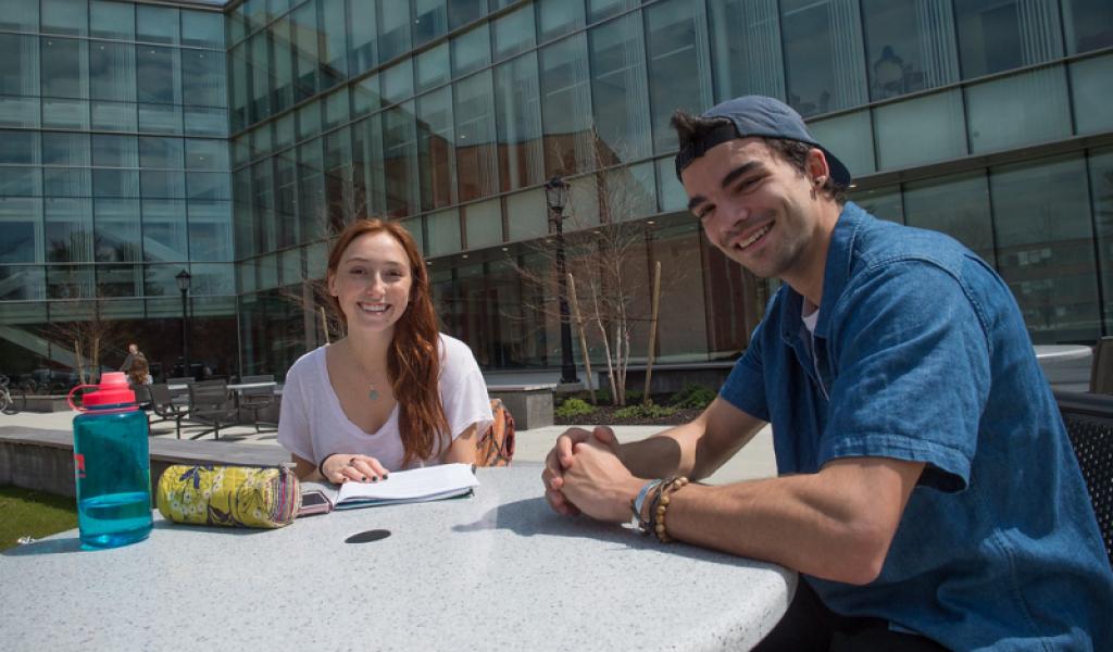 Male and female students smile toward camera as they sit in the Stevens Center courtyard in the sun