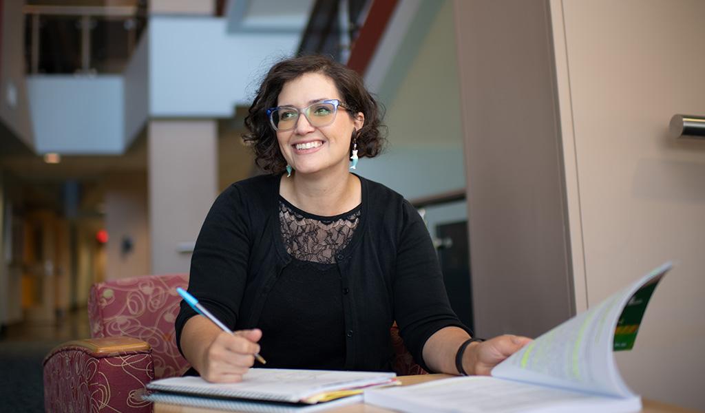 A person turns pages in a book while taking notes.