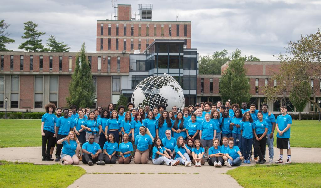 Urban Education group photo in front of campus globe with students wearing blue tee shirts.