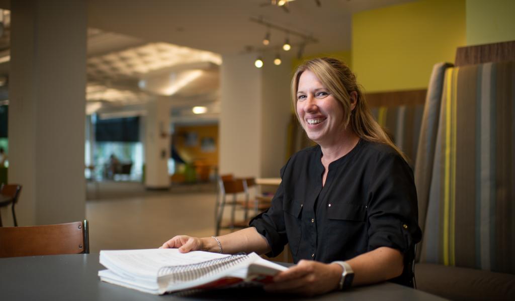 Master of Education student smiling with blonde shoulder length hair and notebook in front of her.