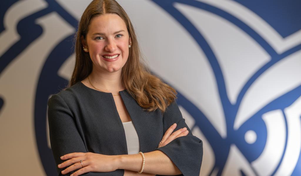 Student smiling confidently with arms crossed, standing in front of the WSU owl logo.