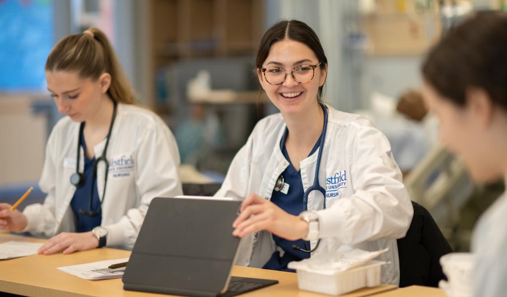 Smiling nursing student opening a laptop in a classroom.
