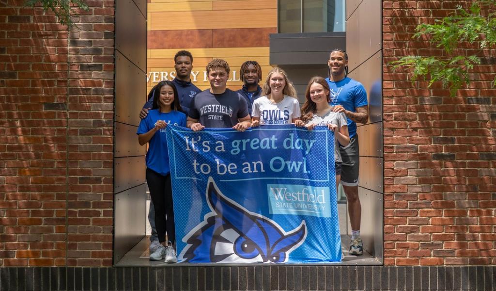 Students hold an “It’s a Great Day to Be an Owl” flag on the campus green.