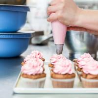 Cupcakes being decorated with pink icing.