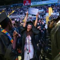 Students cheer and raise their diplomas at commencement.