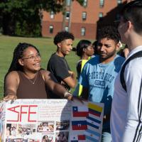 Students gathered around a "Latinx" poster, one with dark hair and glasses, one in a blue t-shirt, and another in a long, white sleeved t-shirt.