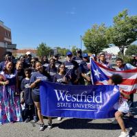 Representatives of Wesfield State wearing navy blue t-shirts and holding Westfield State University banners, as well as the Puerto Rican flag.
