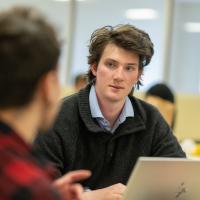 Student in front of laptop wearing grey shirt.