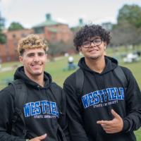 Two students wearing Westfield State University sweatshirts smile while on the campus green.