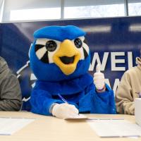 Blue owl mascot shows a thumbs up while two students write notecards