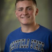 Matt Crusha ’27 smiles for a portrait while wearing a blue Westfield State University T-shirt.